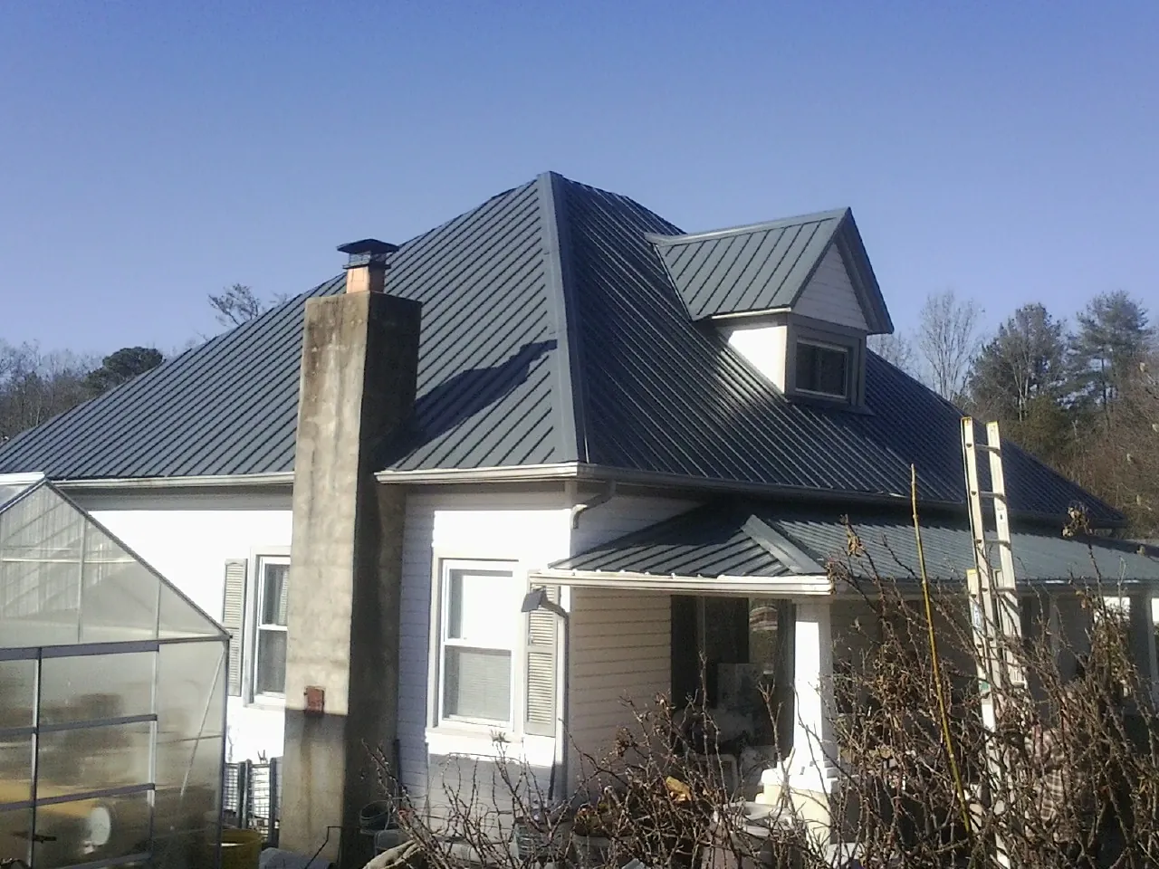 Dark blue standing seam metal roof on a white farmhouse with dormer in Brownsville