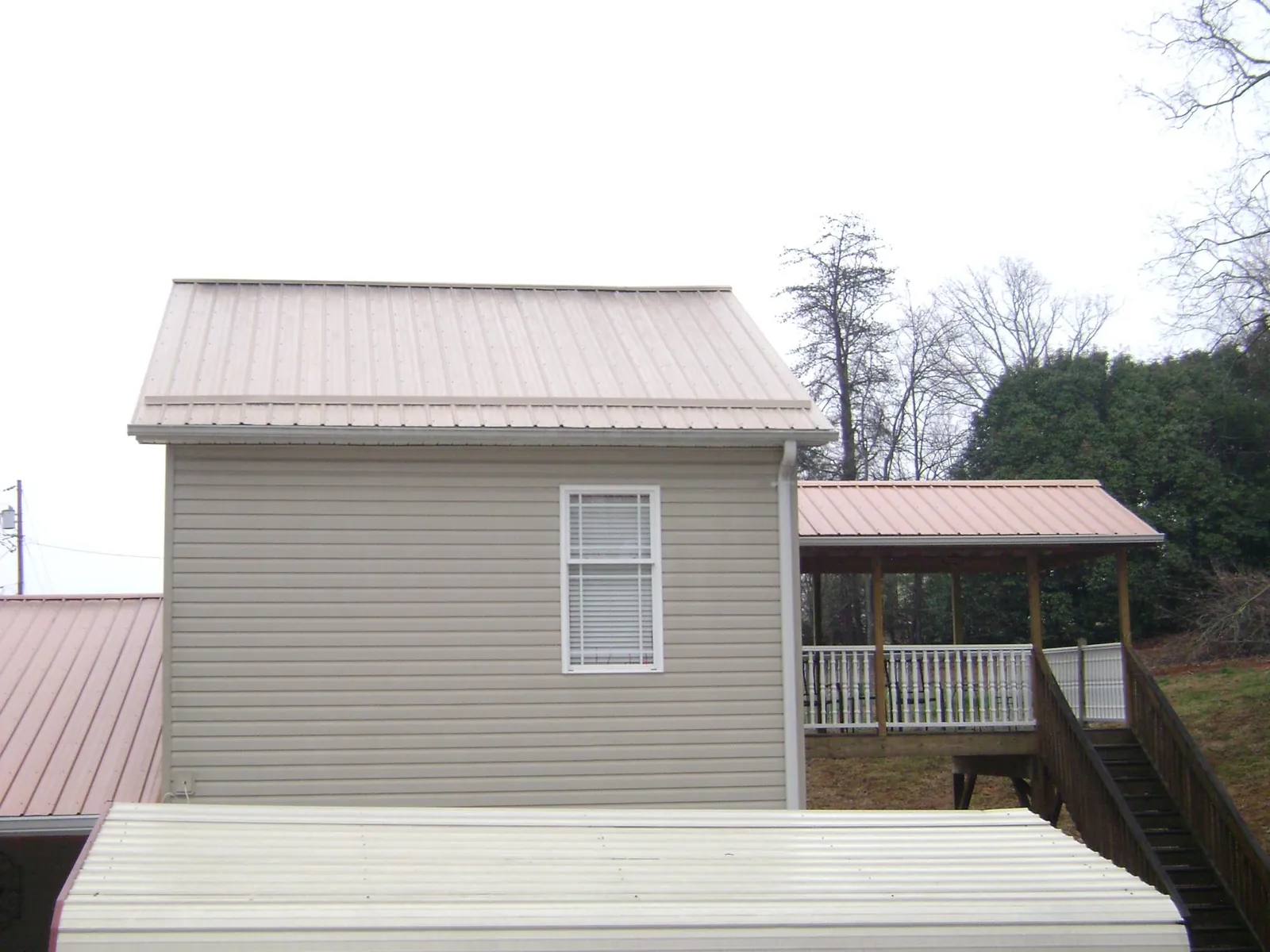 Tan metal roofs on a two story addition and attached porch, from a Roof Replacement job in Brownsville